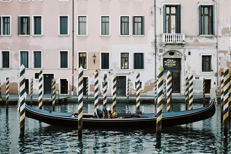 A gondola moored to striped poles before pastel facades in Venice