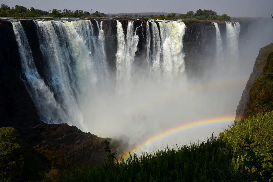 Water pouring over the cliff at Victoria Falls with a rainbow in the spray
