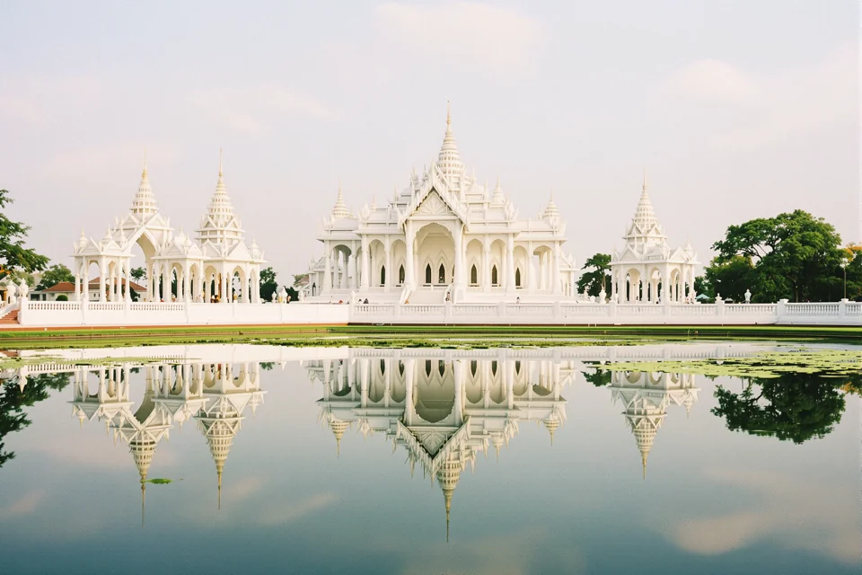 White multi-spired Thai temple mirrored in the still pond that fronts its terrace