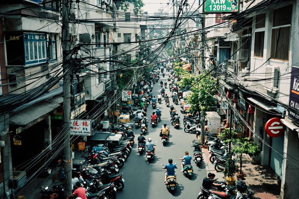 A street in Vietnam seen from above, full of motorbikes and webbed with power lines