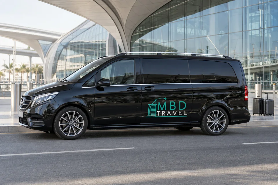 Black Mercedes-Benz Vito private transfer vehicle with MBD Travel livery at airport arrivals beside luggage, visualization